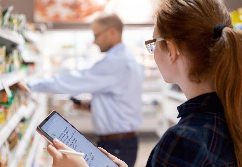 Innerhalb eines User-Research beobachtet eine Person einen Supermarkt-Mitarbeiter und macht sich Notizen auf dem Tablet.
